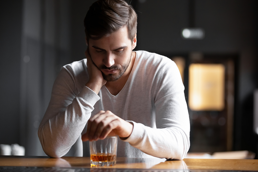 Ein Mann sitzt bedrückt an einem Bartresen und starrt in ein mit Alkohol gefülltes Glas.
