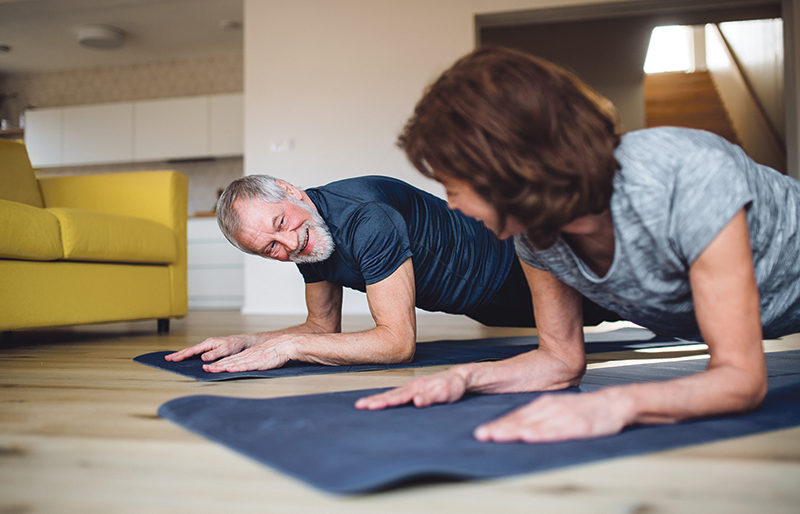 Ein älteres Paar macht auf einer Yogamatte Krafttraining.