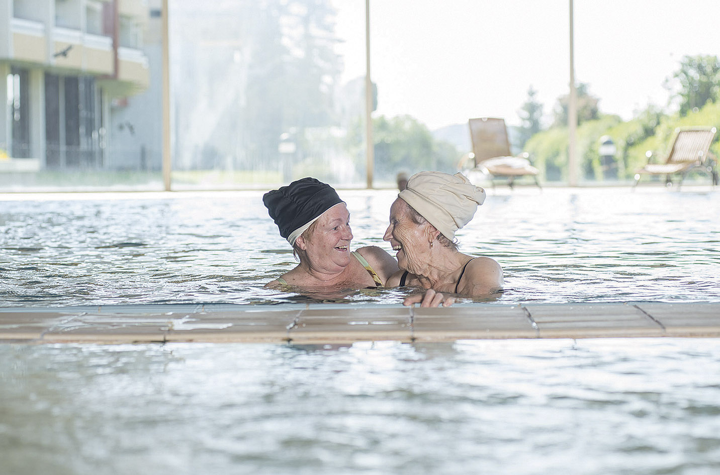 Zwei Rentnerinnen lächeln sich im Schwimmbecken an.