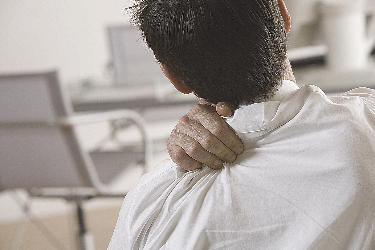 Mann fässt sich an seine Schulter wegen Schmerzen. Thema: Ergonomischer Arbeitsplatz