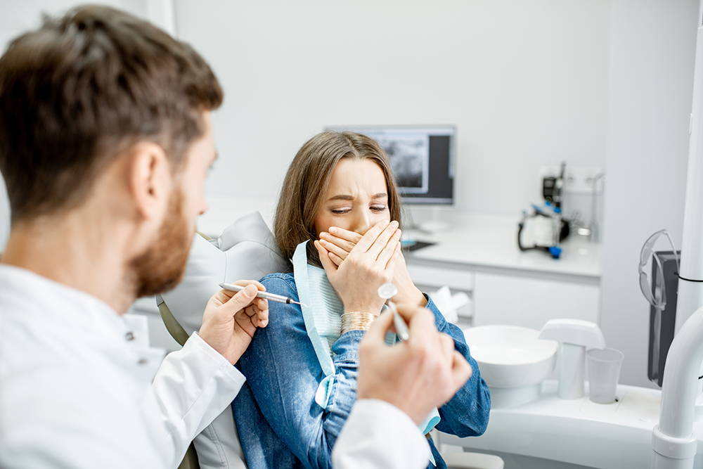 Eine Frau hält sich beim Zahnarzt angsterfüllt den Mund zu.