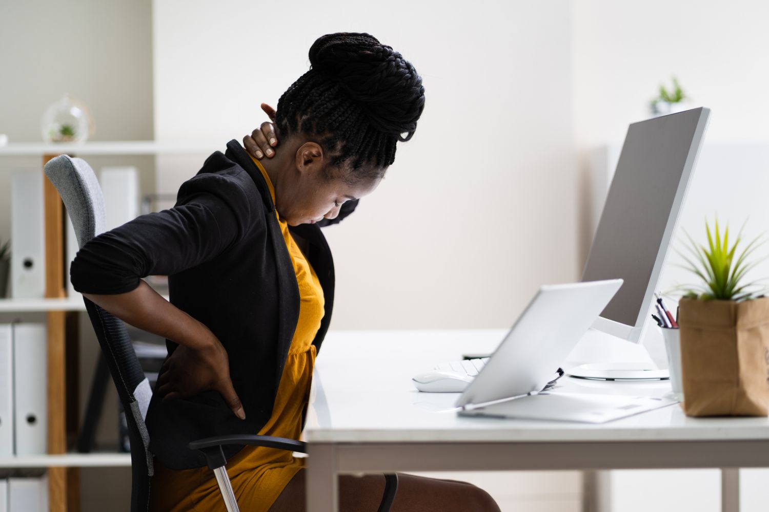 Junge Frau sitzt am Schreibtisch und fässt sich in den Nacken aufgrund von Rückenschmerzen