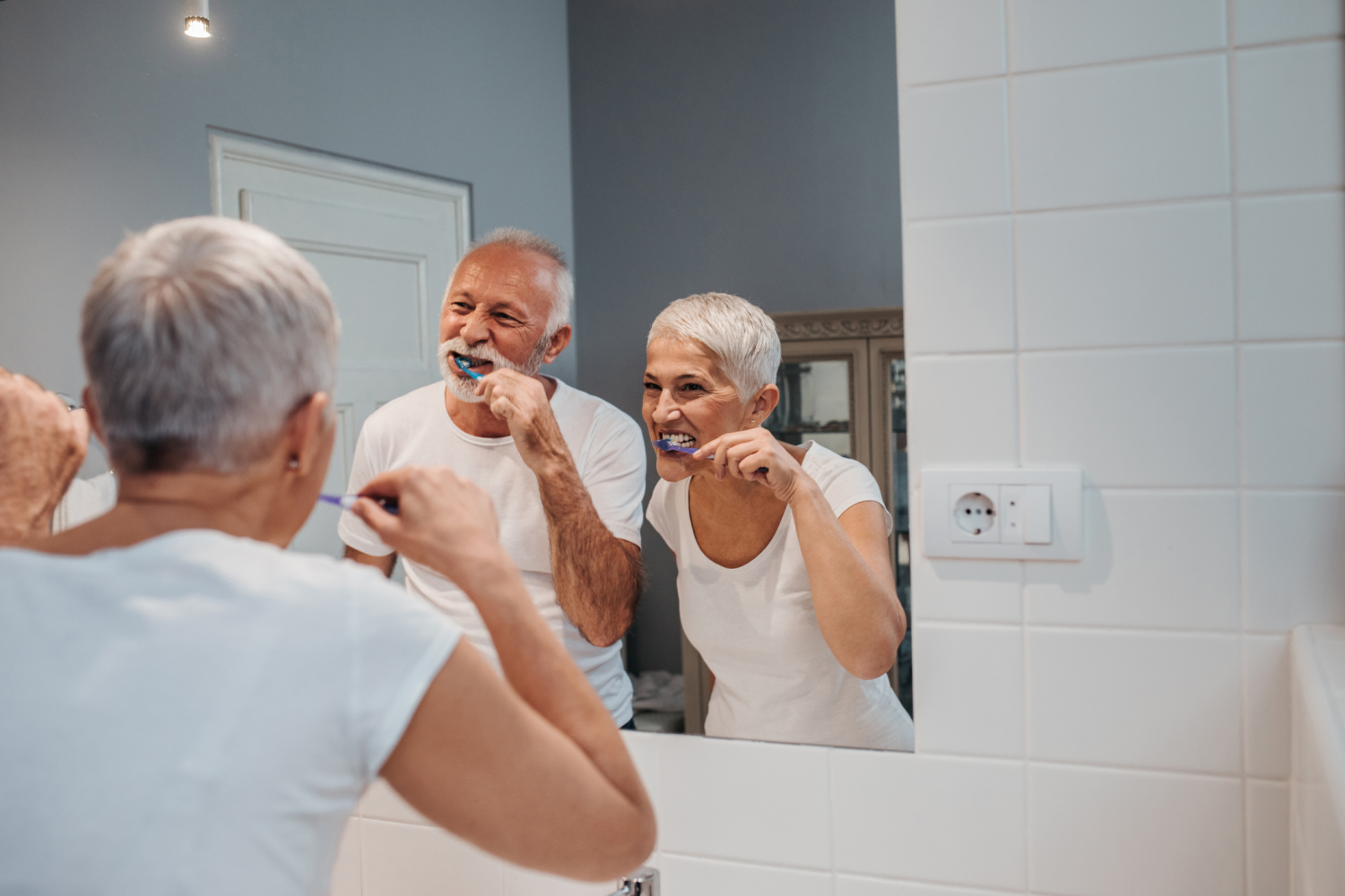 Ein älteres Paar steht beim Zähneputzen im Bad vor einem großen Spiegel.