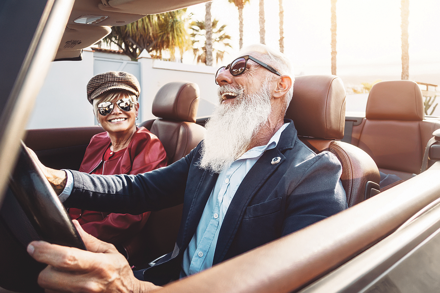 Zwei ältere Menschen sitzen lachend in einem Cabrio.