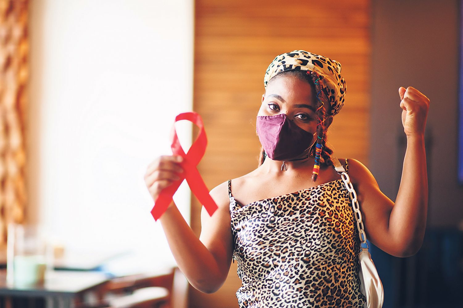 Ein Mädchen hält eine rote Schleife als Symbol für Solidarität mit HIV-Infizierten und streckt eine Faust in die Luft.